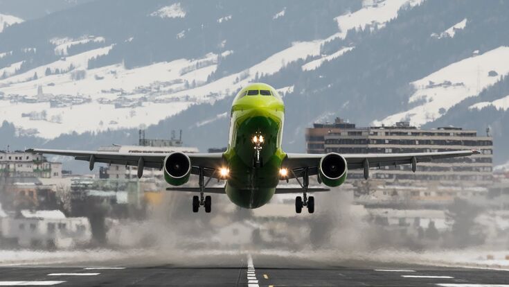 frontansicht auf grünes passagierflugzeug beim Abheben am flughafen innsbruck, im hintergrund die berge und schnee