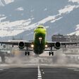 frontansicht auf grünes passagierflugzeug beim Abheben am flughafen innsbruck, im hintergrund die berge und schnee
