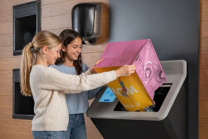 zwei mädchen entleeren leergut aus einer großen einkaufstasche in eine pfandrückgabemaschine von tomra