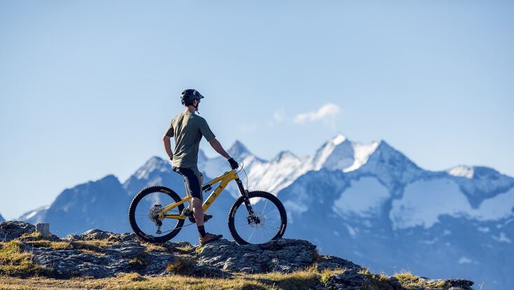 junger schlanker mann auf e-montainbike auf einer grünen anhöhe, panorama auf tiroler berge