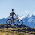 junger schlanker mann auf e-montainbike auf einer grünen anhöhe, panorama auf tiroler berge