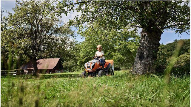 junge person mit gehörschutz fährt Rasentraktor von Stihl durch grüne, naturbelassene wiese