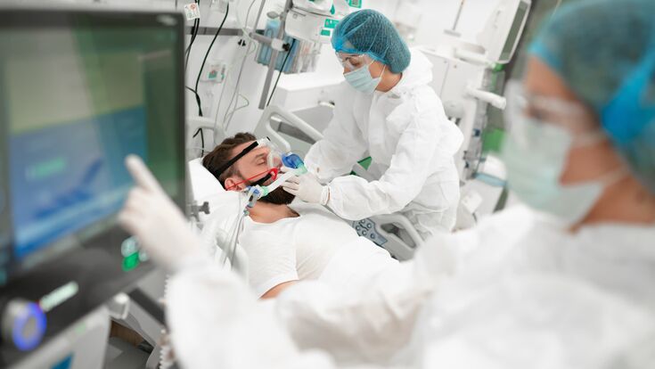 ein mann bekommt bei einer OP eine maske aufgesetzt, eine weitere medizinische fachkraft tippt auf monitor