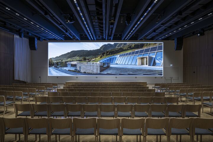Frontalansicht auf viele leere Sesselreihen vor riesiger LED-Panoramawall im Plenarsaal des Congress Centrum Alpbach