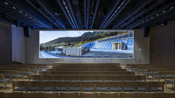 Frontalansicht auf viele leere Sesselreihen vor riesiger LED-Panoramawall im Plenarsaal des Congress Centrum Alpbach