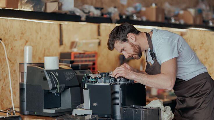 mann repariert in unaufgeräumtem umfeld eine kaffeemaschine