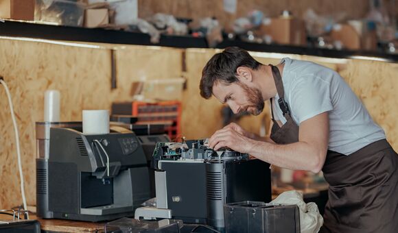 mann repariert in unaufgeräumtem umfeld eine kaffeemaschine