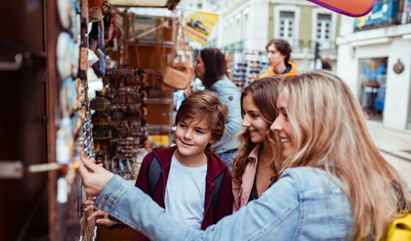 junge mutter und zwei teeander-kinder shoppen an marktstand nach souvenir-magneten