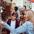 junge mutter und zwei teeander-kinder shoppen an marktstand nach souvenir-magneten
