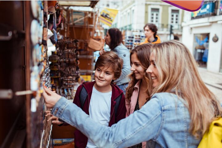 junge mutter und zwei teeander-kinder shoppen an marktstand nach souvenir-magneten