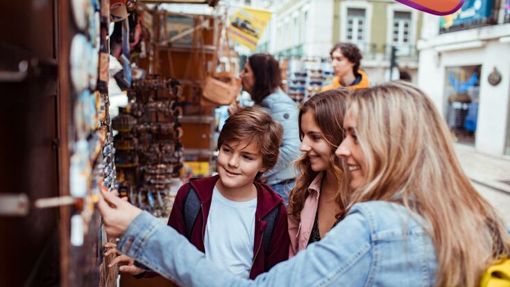junge mutter und zwei teeander-kinder shoppen an marktstand nach souvenir-magneten