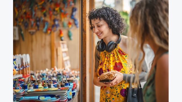 Eine junge Frau in Sommerkleid und Kopfhörern shoppt an Marktstand nach buntem keramik