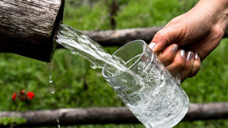 hand mit lackierten nägeln lässt einen starken wasserstrahl aus einem holzrohr in einen bierkrug laufen