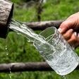 hand mit lackierten nägeln lässt einen starken wasserstrahl aus einem holzrohr in einen bierkrug laufen