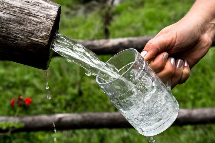 hand mit lackierten nägeln lässt einen starken wasserstrahl aus einem holzrohr in einen bierkrug laufen