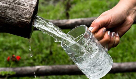 hand mit lackierten nägeln lässt einen starken wasserstrahl aus einem holzrohr in einen bierkrug laufen
