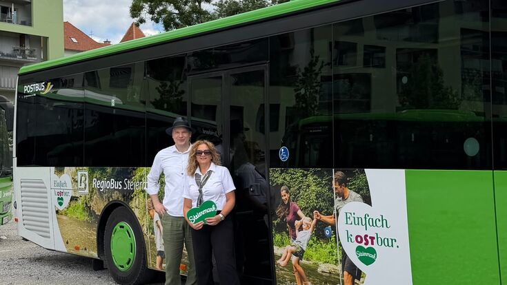 Stefan Schindler (GF Tourismusverband Oststeiermark) und Eveline Trummler (Postbus Junior-Disponentin) vor einem mit werbung für die oststeiermark versehenem regiobus