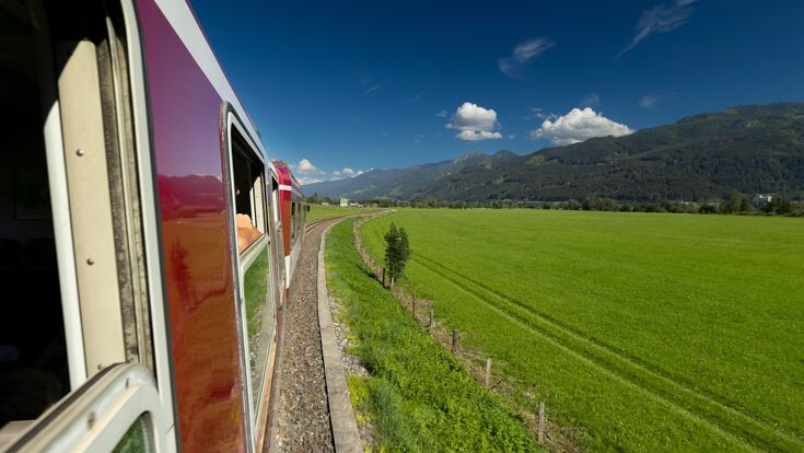 blick aus pinzgauer lokalbahn auf grüne wiese unter blauem himmel, teil der bahn sichtbar