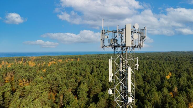 hoher telekommunikationsturm mit antennen für 5G in großem dichten wald unter blauem himmel