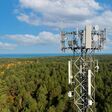 hoher telekommunikationsturm mit antennen für 5G in großem dichten wald unter blauem himmel